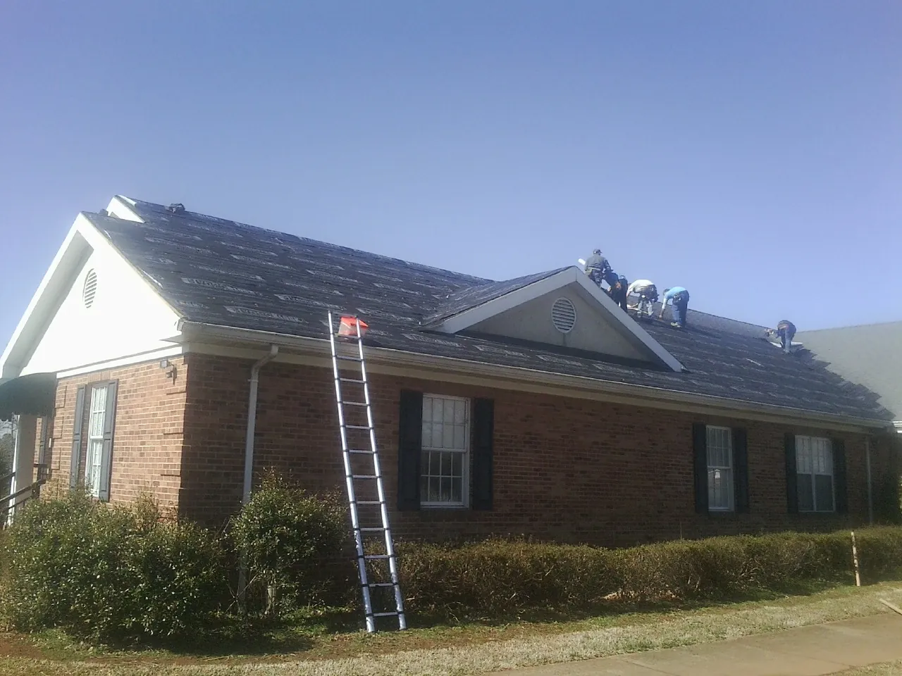 Crew tearing shingles off a brick ranch roof with a ladder set — Emergency Roof Repair work by our crew in Gruetli Laager