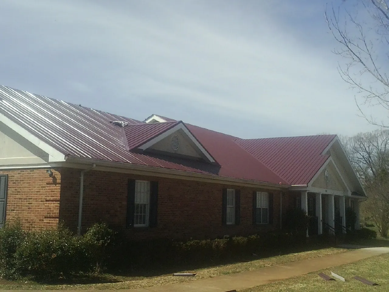 Red metal roof with gabled entries on a long brick building, from a Hail Damage Roof Repair job in Gruetli Laager