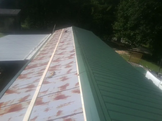 Old rusted panels beside newly installed green metal roofing in Gruetli Laager