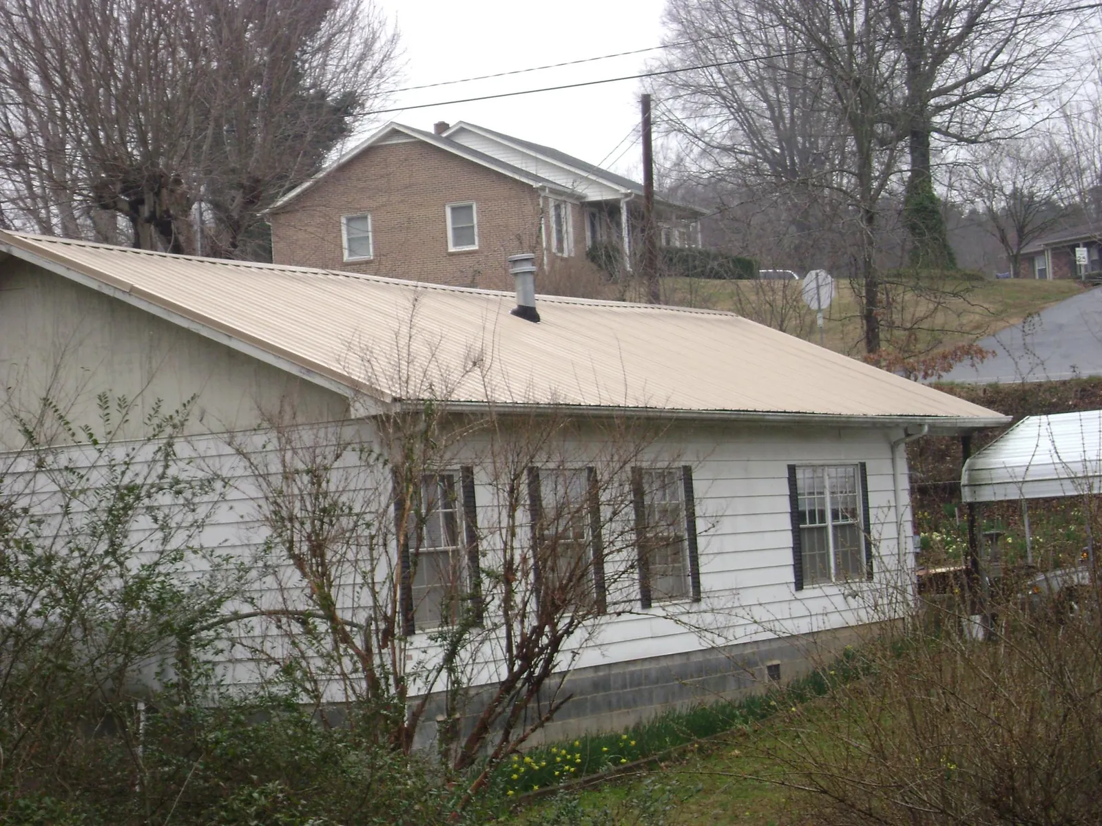 Tan metal roof on a white sided house set into a hillside — Commercial Roofing by Roofing Brothers in Gruetli Laager