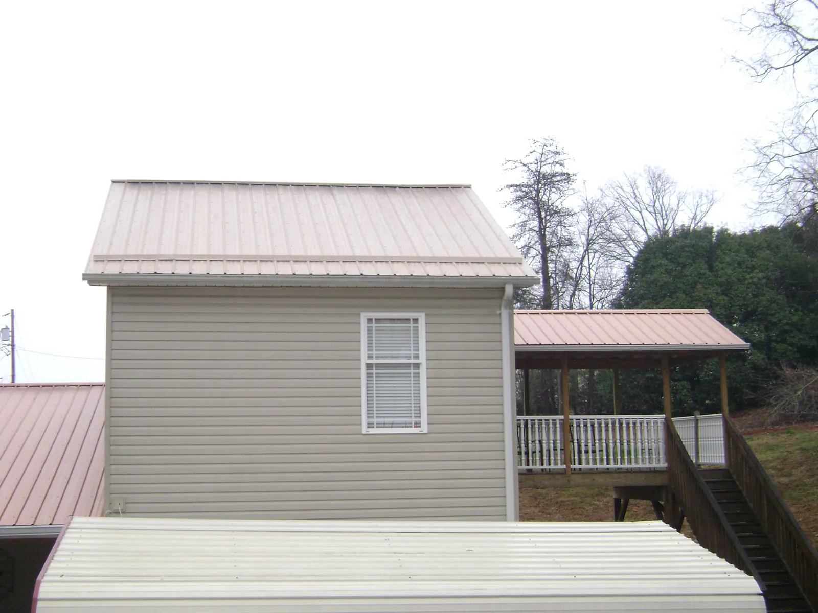 Tan metal roofs on a two story addition and attached porch, from a Roof Replacement job in Gruetli Laager
